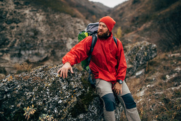 outdoors portrait of tired hiker man in red clothes sitting on the rock relaxing after hiking in mou