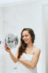 Wall Mural - Skin care. Woman touching hair and smiling while looking in the mirror.Portrait of happy girl with wet hair in bathroom