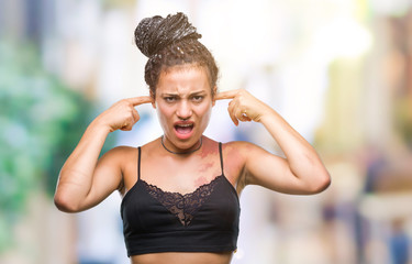 Wall Mural - Young braided hair african american with pigmentation blemish birth mark over isolated background covering ears with fingers with annoyed expression for the noise of loud music. Deaf concept.