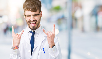 Sticker - Young professional scientist man wearing white coat over isolated background shouting with crazy expression doing rock symbol with hands up. Music star. Heavy concept.