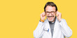 © Krakenimages.com - Middle age doctor men wearing medical coat covering ears with fingers with annoyed expression for the noise of loud music. Deaf concept.