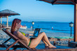 © Михаил Решетников - A young woman is sitting on a deck chair with a laptop next to the sea. Work in travel. Freelancer