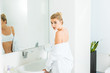 © LIGHTFIELD STUDIOS - selective focus of attractive and blonde woman in bra and white bathrobe looking at camera in bathroom