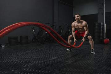 Man wear red shorts doing battle ropes exercise at the crossfit gym