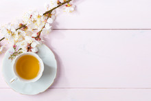 Cup Of Tea And Spring Flowers (blooms Of An Apricot) On A Light Pink Wooden Table.