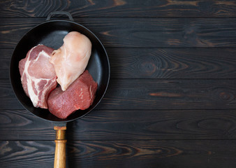 raw different meat on black cooking pan, top view. Wooden background. 