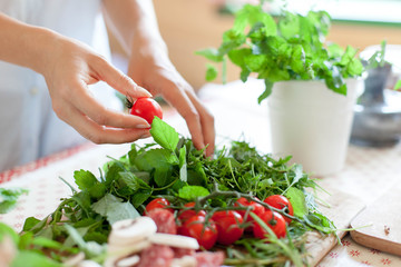 Woman is cooking in home kitchen. Female hands choose cherry tomatoes, vegetables for recipe. Ingredients for preparing italian or french food are on table on wooden boards. Lifestyle moment. Close up