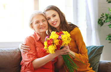 happy mother's day! adult daughter gives flowers and congratulates an elderly mother on holiday