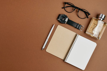 Set of stylish male accessories with a pen, perfume, clock, notepad and glasses on brown background. Minimal concept Fathers Day . Flat lay, top view, copy space