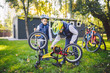 © Elizaveta - Two children, older boys and younger brother learning repair bike. Two guys siblings in helmets and single clothes use pump tool and pump air into bicycle wheel in park background of the house