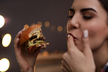 Young Woman Eating Tasty Burger In Cafe