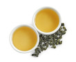 Cups of Tie Guan Yin oolong and tea leaves on white background, top view