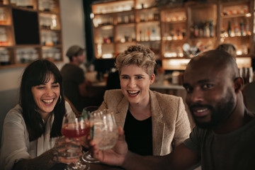 Wall Mural - Smiling friends cheering together with drinks at a bar table