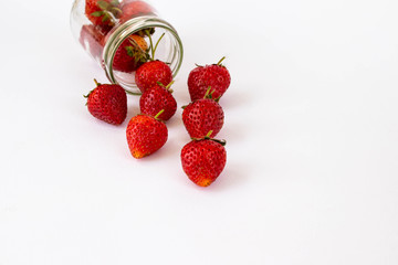 Strawberrys many with both ripe fruit and  not fruit ripe in jar glass and strawberrys outside jar all laid are on a white background.