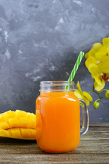 Wall Mural - Mango smoothie in a glass jar and fresh mango on a wooden background. Mango shake. Tropical fruit concept.