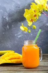 Wall Mural - Mango smoothie in a glass jar and fresh mango on a wooden background. Mango shake. Tropical fruit concept.