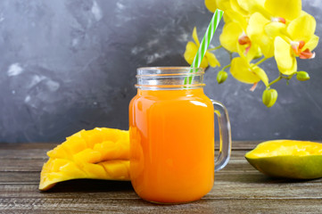 Wall Mural - Mango smoothie in a glass jar and fresh mango on a wooden background. Mango shake. Tropical fruit concept.