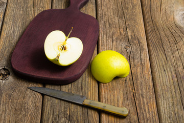 half cut green apples on chopping board, knife, old wooden table