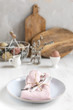 Easter table setting idea, minimal decoration - pink napkin, fork, coloured eggs in white basket, willow banch, wooden cutboard