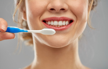 oral care, dental hygiene and people concept - close up of smiling woman with toothbrush cleaning teeth over gray background