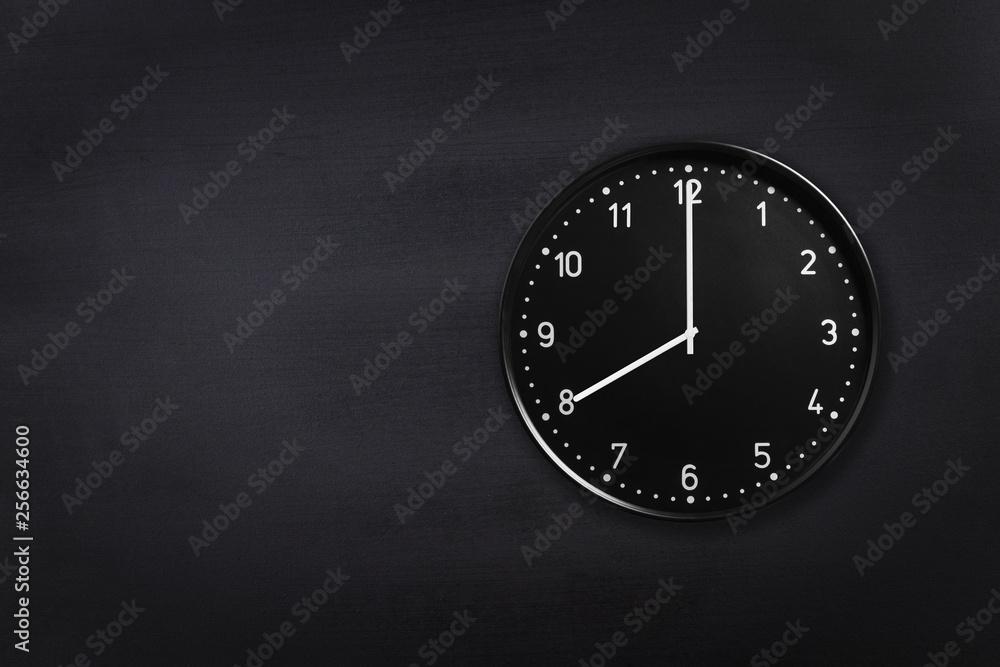 Black wall clock showing eight o'clock on black chalkboard background. Office clock showing 8am or 8pm on black texture