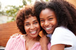 Middle aged black mum and teenage daughter embracing and smiling to camera