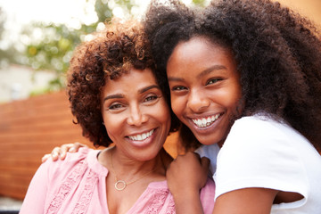 middle aged black mum and teenage daughter embracing and smiling to camera