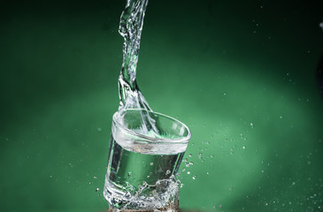 falling small transparent glass with clear water and spilling water on a green background