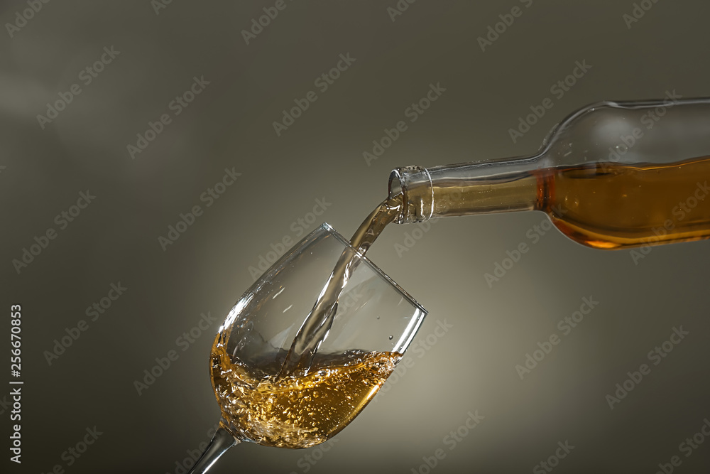 Pouring of wine into glass on color background