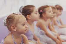Close Up Of A Beautiful Little Ballerina Girl Sitting With Her Classmates At Ballet School. Group Of Cute Little Girls At Dance Studio. Children, Kids, Childhood Concept
