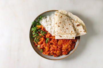 Wall Mural - Vegan vegetarian curry with ripe yellow jackfruit served in ceramic bowl with rice, coriander and homemade flatbread flapjack over white marble background. Flat lay, space