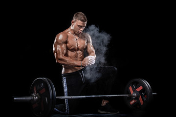 Photo of strong muscular bodybuilder athletic man pumping up muscles with barbell on black background. Workout energy bodybuilding concept.