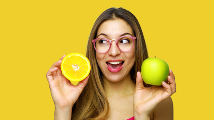 Happy funny girl presenting fruits looking to the side against orange background