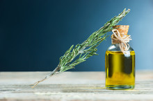 Bottle Glass Of Essential Rosemary Oil With Dry Rosemary Branch On Wooden Background. Herbal Oil Concept