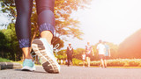 Fototapeta  - Young fitness woman legs walking with group of people exercise walking in the city public park in morning.