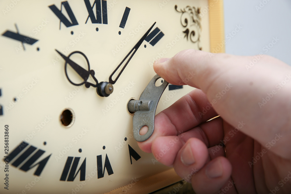 the hand holding the wind-up key in clock. the hand winds old clock by  clockwork