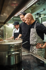 Wall Mural - Great job. Cheerful professional chef looking how his two assistants are cooking in a restaurant kitchen