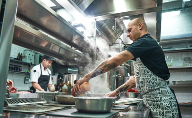 Wall Mural - How to cook a meat Concentrated young chef in apron and cooks preparing food together in a restaurant kitchen