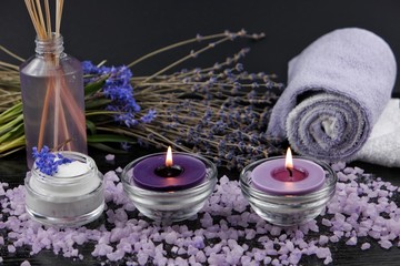  Burning aromatic candles, dry lavender, cosmetics on a black wooden table. Spa and aromatherapy accessories