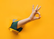 Hand OK sign. The teenage hand came out into the hole of yellow paper and shows symbol of Okay. Copy space, fine.