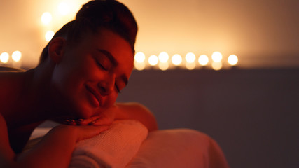 Woman relaxing after massage in dark room with candles