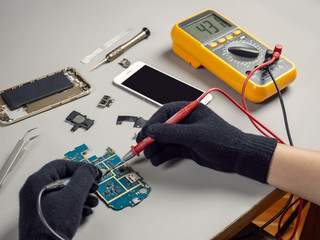 Technician or engineer using digital multimeter to electric current measurement on smartphone logic board for diagnosis broken smartphone 