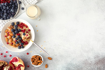 Healthy breakfast ingredients on grey concrete background, flatlay. Bowl of oat flakes with milk, fresh berries, nuts and fruits. Top view, copy space