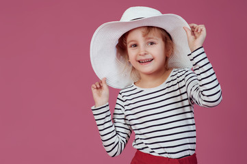 Happy little girl in white hat at pink studio background.