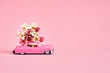 Pink toy car delivering flowers bouquet on pink backgroun. Flower delivery concept. Copy space