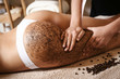 Close up of woman getting buttocks and legs massage with coffee scrub at spa. Using coffee beans for perfect skin and body.