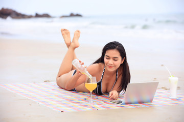 sexy woman line down on beach with happy drink and play laptop on her vacation