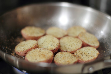 Red potato potato chips cooking in a stainless steel pan.