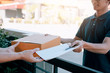 © wutzkoh - Young asian man smiling while delivering a cardboard box to the woman holding document to signing signature.