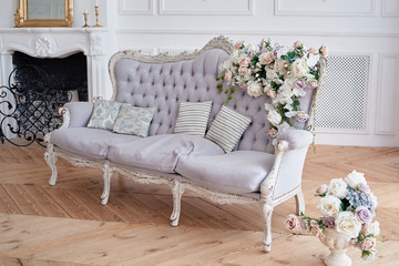 Wall Mural - Soft sofa with gray fabric upholstery, pillows and flowers, copy space. Luxury rich living room interior with elegant vintage textile couch and fireplace. Chesterfield upholstery